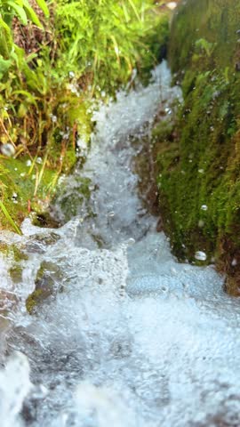 Water rushing through narrow channel with mossy walls. Close up of white water rapids and spray flowing through a small narrow moss covered gorge or irrigation canal.