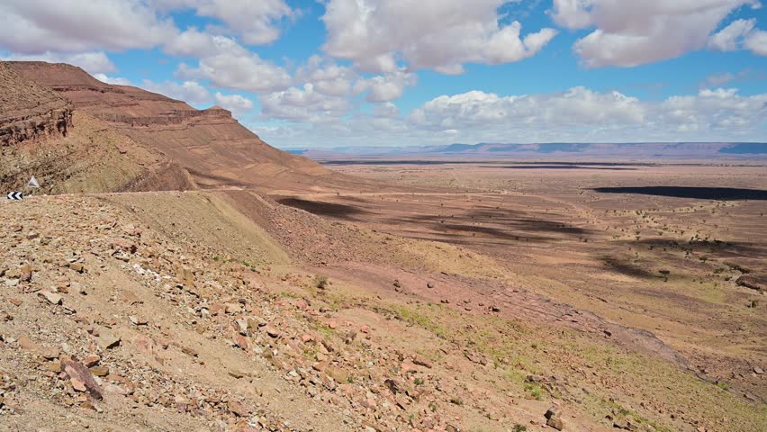 Vast arid landscape with mountains and cloud shadows moving over the terrain in Morocco, near the Sahara Desert. A sunny day with blue sky
