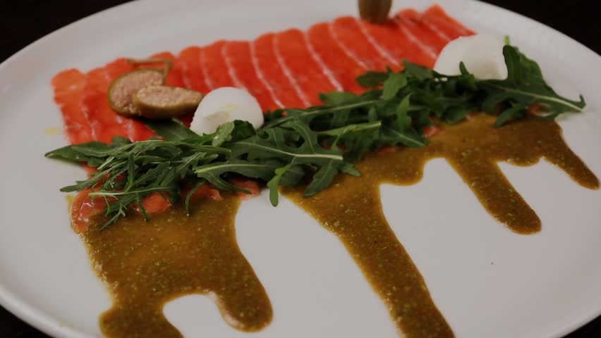A dish of sliced red fish with sauce, herbs and bread