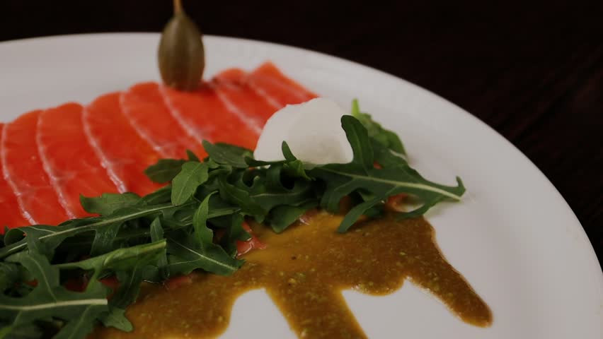 A dish of sliced red fish with sauce, herbs and bread