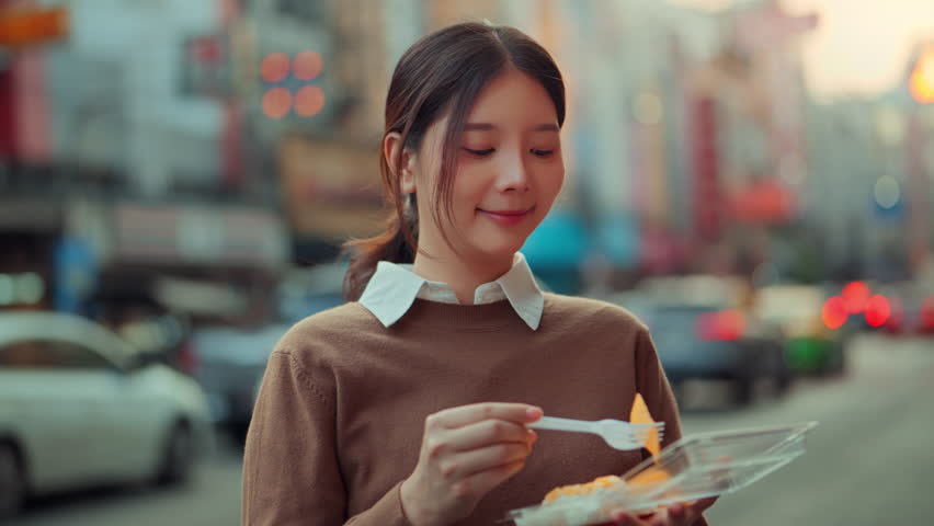 Young Southeast Asian woman eating authentic Thai mango sticky rice at Yaowarat Chinatown, Bangkok. Candid evening street food experience with bokeh lights, highlighting Gen Z travel lifestyle and local culinary tourism in Thailand.