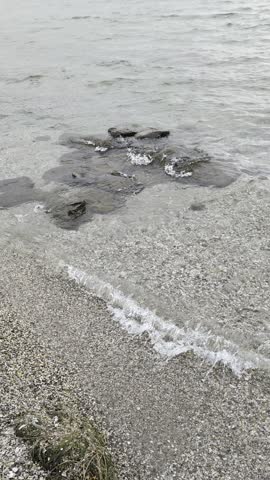 Autumnal lakeshore with washed-up sand and leaves, water with waves.