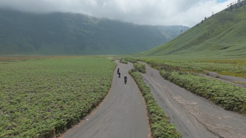 Aerial view of a group of friends riding motorcycles on a scenic road through the green savanna valley in bromo, east java, indonesia