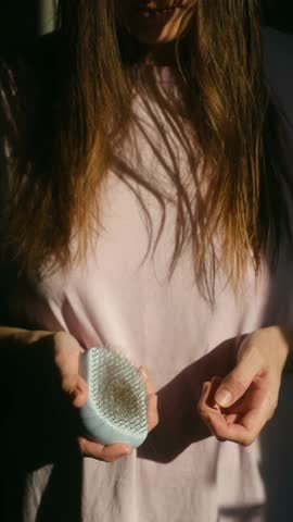 Worried woman pulling large clump of hair from her head after brushing, illustrating emotional distress and symptoms of alopecia, hair loss, and telogen effluvium disease. Vertical