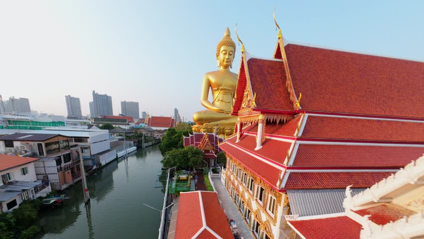 Cinematic FPV drone fly around giant golden Buddha at Wat Paknam temple in Bangkok, Thailand. Aerial movement over city skyline and Buddhist landmark.