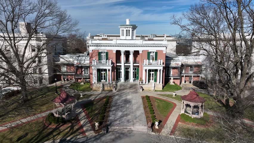 Historic Belmont University building in Nashville during winter with bright sunlight, classic columns, landscaped courtyard and clear blue sky. Aerial approaching shot.