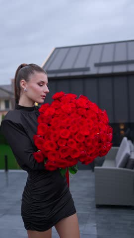 A romantic woman in a black dress holds a large bouquet of roses. The concept of a woman with a bouquet of flowers.