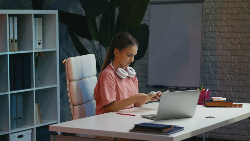 Pleased teen girl calculating budget at desk, saving money for her dream