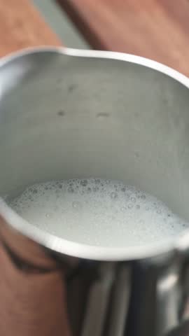 Barista Tapping Milk Pitcher to Stabilize Foam. Close Up