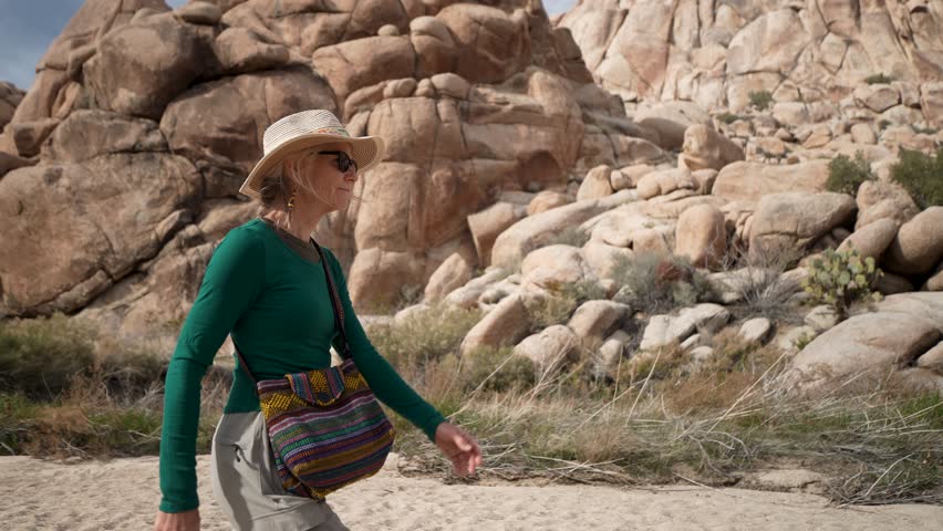 Mature woman walks along the Willow Hole trail in Joshua Tree National Park. She explores the unique rock formations and desert landscape.