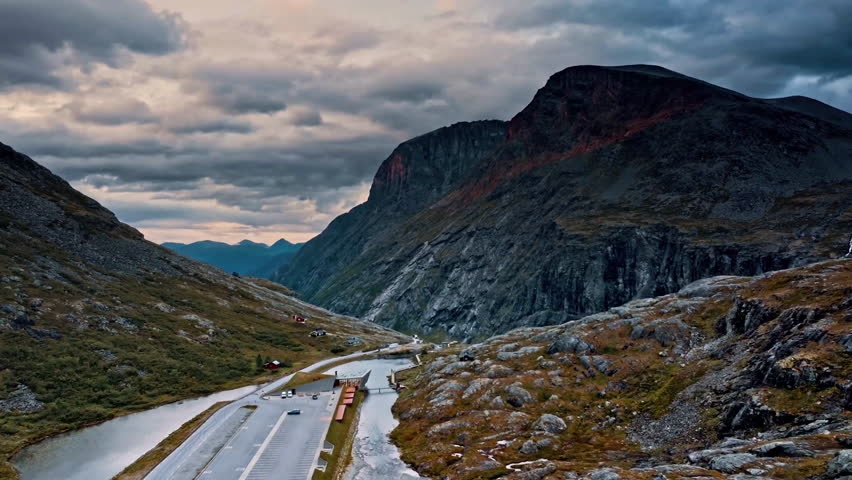 This clip showcases a breathtaking aerial view of a rugged mountain landscape featuring steep cliffs and a winding road. The scene captures the natural beauty and tranquility of the environment under a cloudy sky.