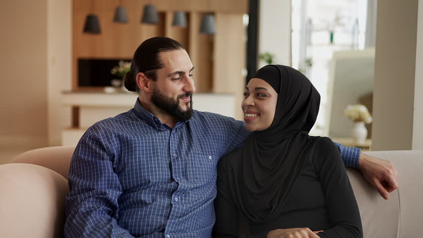 Cheerful Muslim couple showing apartment key, celebrating moving into a new home