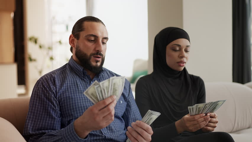 Happy Muslim couple counting dollars and hugging, celebrating finances
