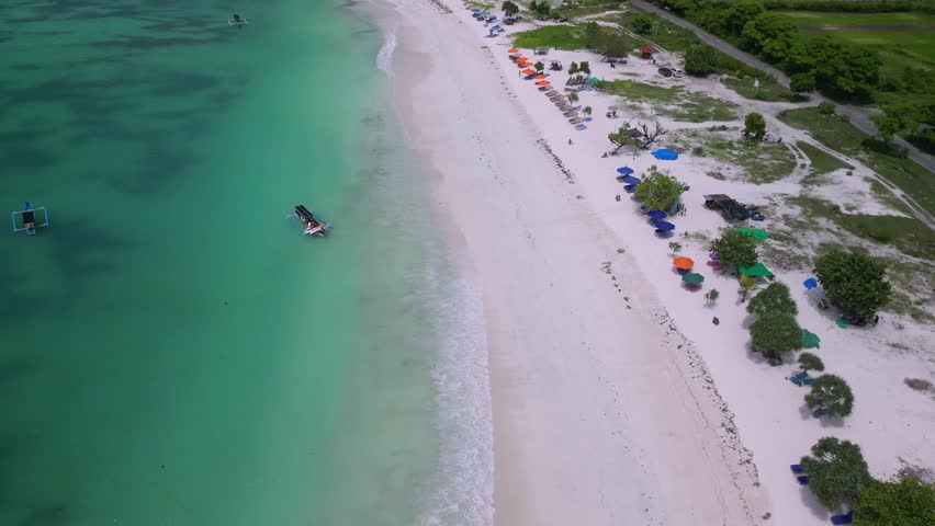 Aerial Tropical Beach Turquoise Water Colorful Umbrellas Lining Sand, Small Boat Cruising Near Shore, Calm Waves Lapping, Sparse Sunbathers Under Parasols, Tanjung Aan,Kuta,Lombok,Indonesia