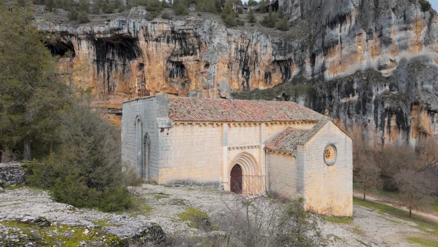 Ancient romanesque chapel nestled among dramatic canyon cliffs and lush vegetation