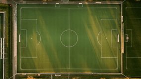 This video captures an aerial perspective of a rectangular football pitch. The visual documents green artificial turf with white painted markings, including the center circle and penalty areas. The composition illustrates a sports facility with goals at opposite ends during sunset, documenting athletic infrastructure and stadium field layout in a high-resolution 4K format for sports and urban planning media. - Powered by Shutterstock - Get 15% off with code: PIKWIZARD15