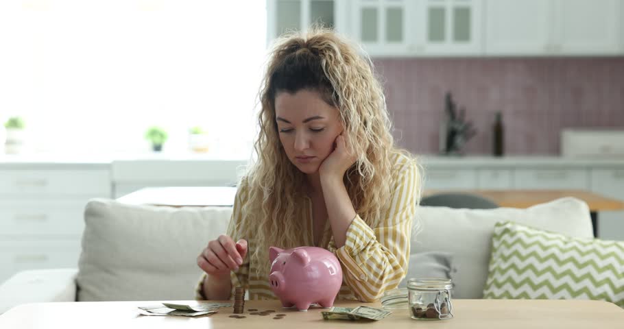 Sad woman with piggy bank and money at wooden table indoors