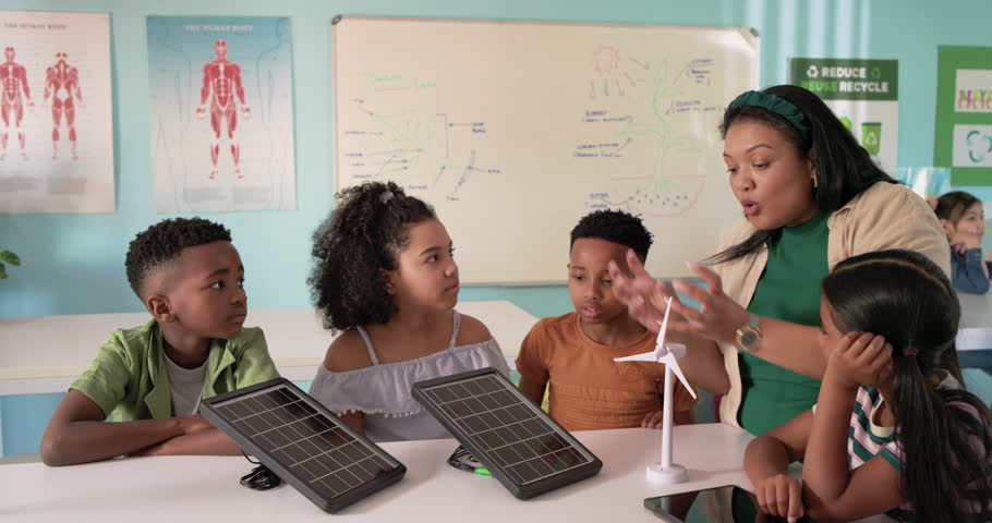African American teacher leading STEM demo with kids at table tapping solar panels to link turbine. Classroom, education, handson, groupwork, science, renewable, energy