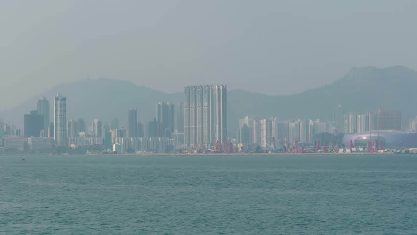 Panoramic view of buildings and skyscrapers from the bay and Victoria Harbour in downtown Hong Kong, China on a sunny day, highlighting the modern skyline.