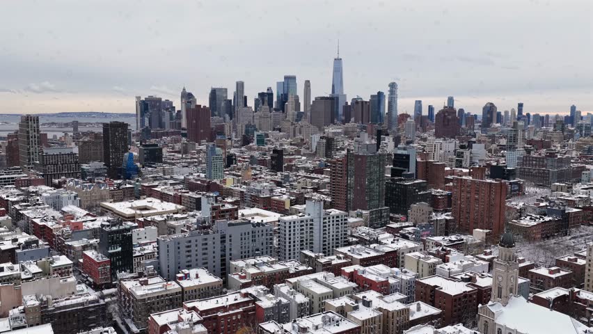Snow flurries flying across Manhattan skyline in winter, revealing dense high-rise architecture, cold gray sky and urban atmosphere over New York City. Aerial wide shot. One World Trade Center in back