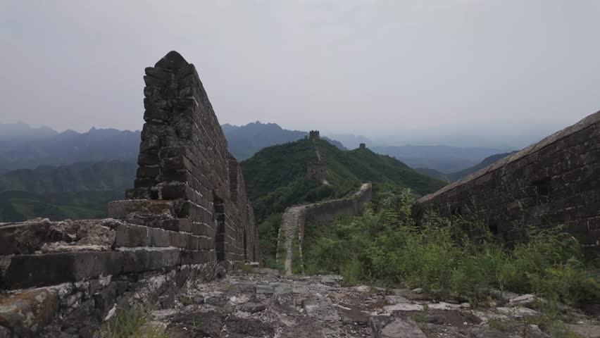 A wide shot of the unrestored wild Great Wall of China winding through green mountains under a misty sky. Perfect for travel documentaries and historical heritage content.