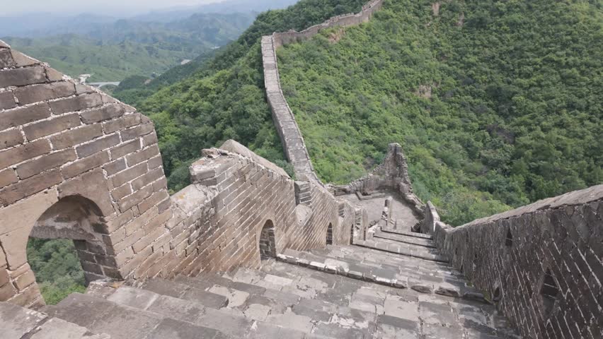 A highangle perspective of the Great Wall of China showing steep stone steps leading towards a distant watchtower on a lush green mountain ridge.