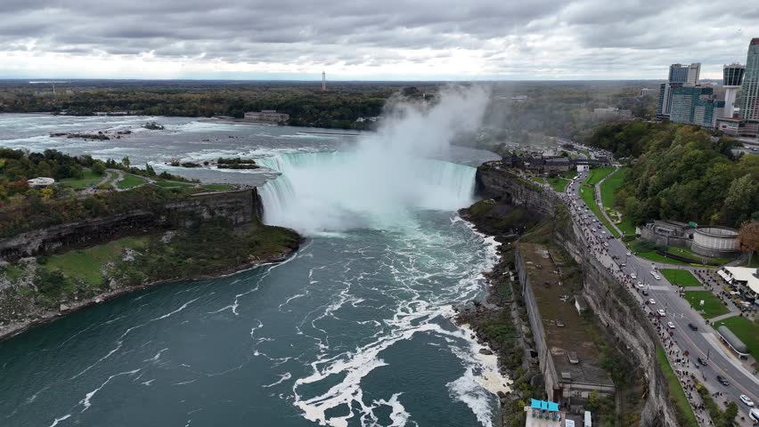 Dramatic aerial view of Niagara Falls with mist rising under a cloudy sky, showcasing natural beauty and tourist attraction, Canada