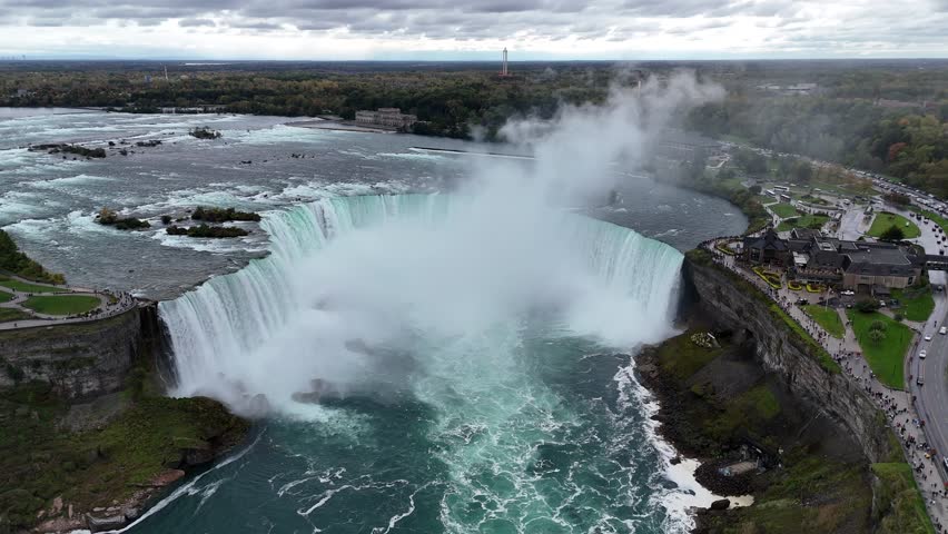 Experience the breathtaking beauty of Niagara Falls on a cloudy day. Tourists walk along the scenic path, taking in the misty veil, Ontario, Canada
