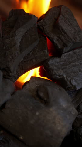 Glowing charcoal burning with bright grill flames, vertical shot of extreme close-up of hot embers and fire heat for barbecue cooking.