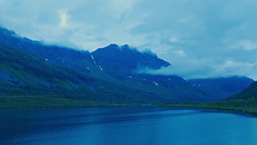 Tranquil Lake With Steep Rugged Mountains Under A Cloudy Sky. Aerial Shot