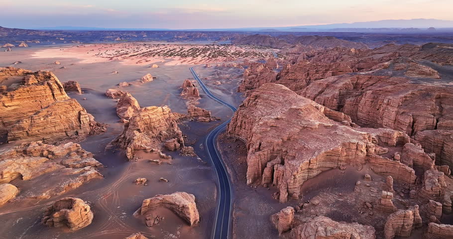 High angle view of a curved highway crossing the unique Yardang geological formations during a golden sunset in Xinjiang, China.