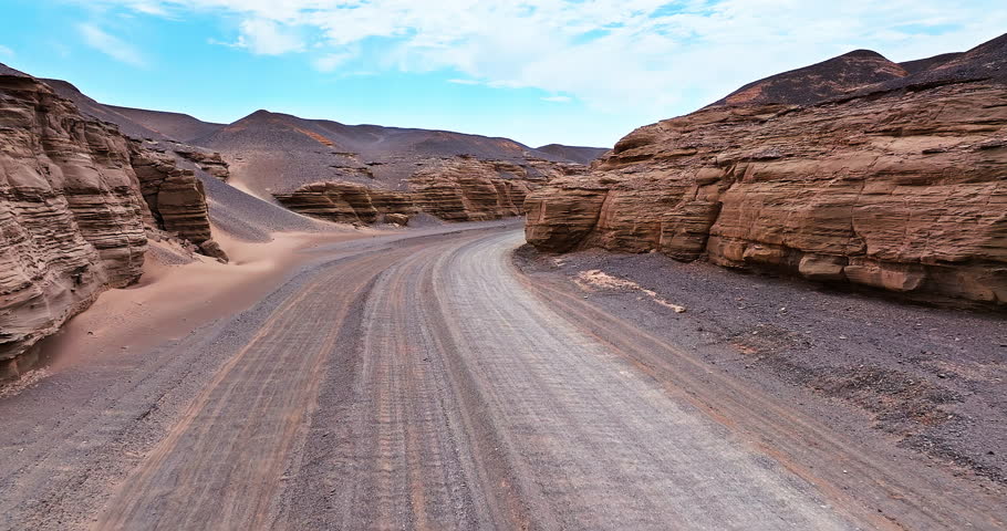 Aerial view of a winding gravel road through dramatic layered Yardang formations in the remote desert of Xinjiang, China.