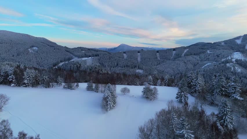 Aerial view of snowy winter mountains and forest under a blue sky