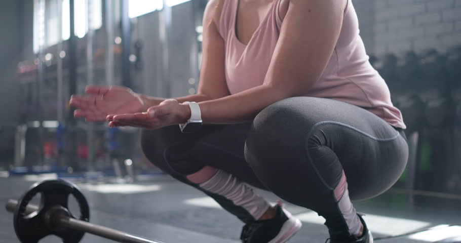 Female lifter in gym is clapping chalk dust gripping barbell lifting to hips bracing next rep. Deadlift, athlete, strength, training, fitness, sunlit, brick