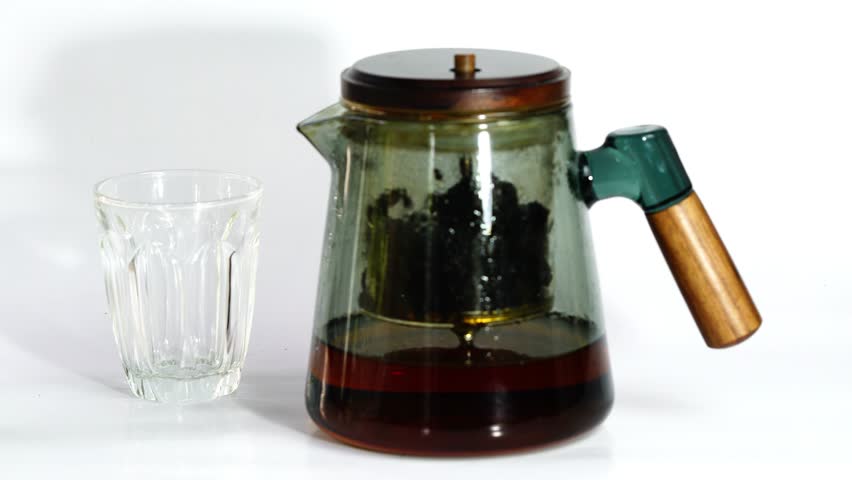 Pouring freshly brewed hot tea fron glass teapot into a small teaglass on white background.