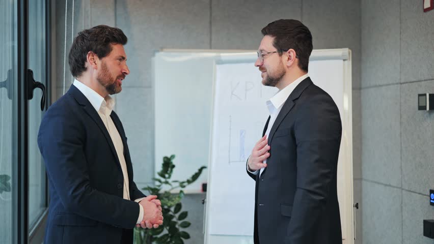 Two businessmen shaking hands in an office, symbolizing a successful partnership. Faces show happiness and confidence, representing agreement and trust in collaboration.