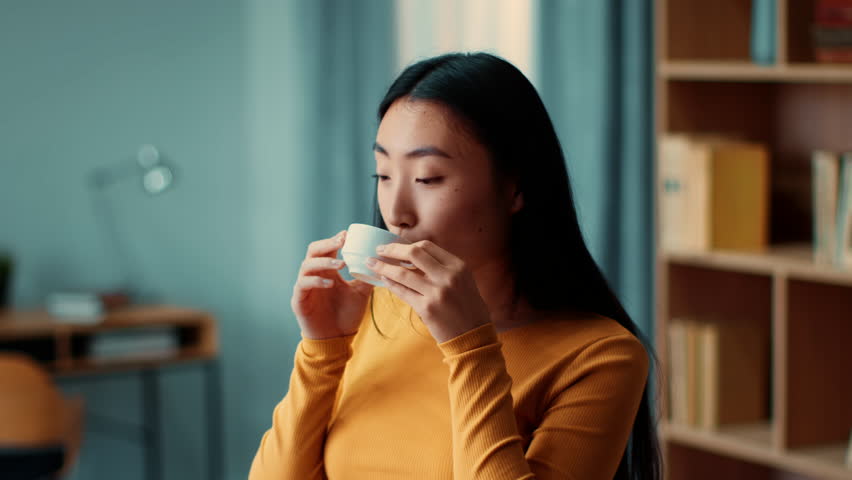 Woman Enjoying a Warm Drink While Sitting in a Cozy Indoor Space With Books Around