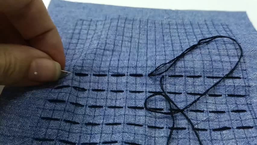 Geometric sashiko embroidery pattern on blue woven fabric. Close-up of decorative sashiko embroidery pattern stitched on blue woven textile surface.