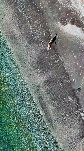 Aerial view of a beautiful young woman with a casual attire dancing with her shadow on the beach in a sunny morning