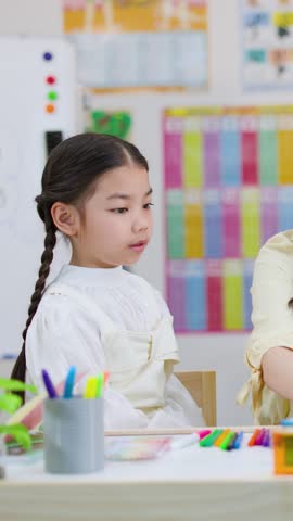 Smiling teacher helps elementary students explore colorful geometric shapes in bright classroom, static medium shot