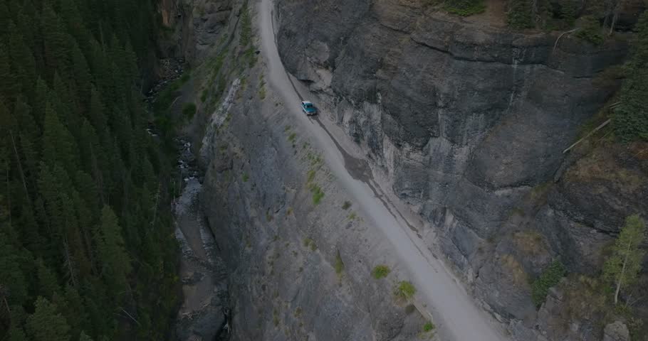 Scenic alpine road entering Yankee Boy Basin near Ouray, solo car drives below overhang, aerial descend