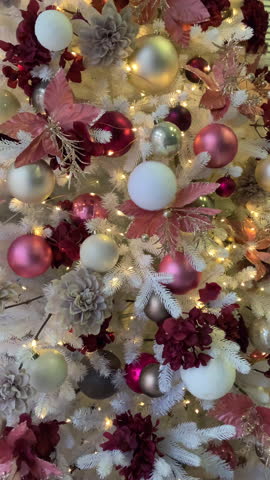 Decorated white artificial Christmas tree with pink burgundy and gold ornaments baubles lights and poinsettia flowers. Festive holiday decor