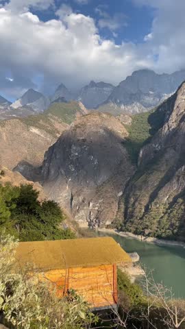 A breathtaking 1080p aerial time-lapse capturing fast-moving clouds and shifting sunlight shadows over a wooden eco-cabin and rugged mountain peaks in Yunnan, China.