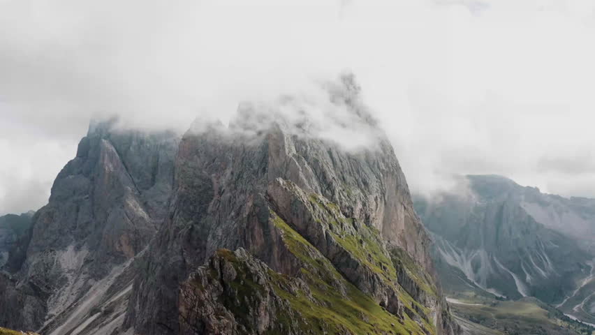 Dramatic mountain landscape featuring towering peaks partially covered by clouds, showcasing the beauty of nature in a serene setting.