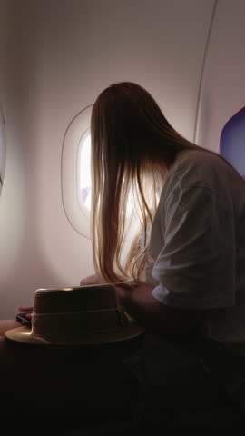 Teenage girl taking photo through airplane window with smartphone.