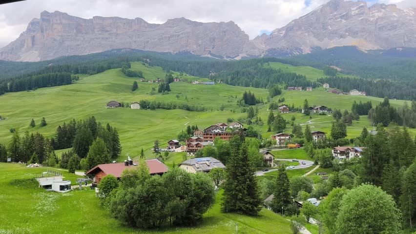 Wide scenic view of alpine landscape with traditional houses, green meadows and dramatic mountain peaks in Alta Badia, La Villa, Dolomites, Italy. Peaceful countryside atmosphere in the Italian Alps.