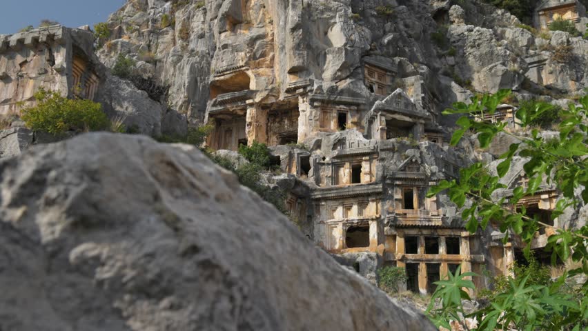 Ancient rock-cut tombs of Myra in Turkey carved into the limestone cliff, detailed view of the Lycian necropolis at daylight. Historic Lycian tombs and architecture in Myra, Turkey. Gimbal shot