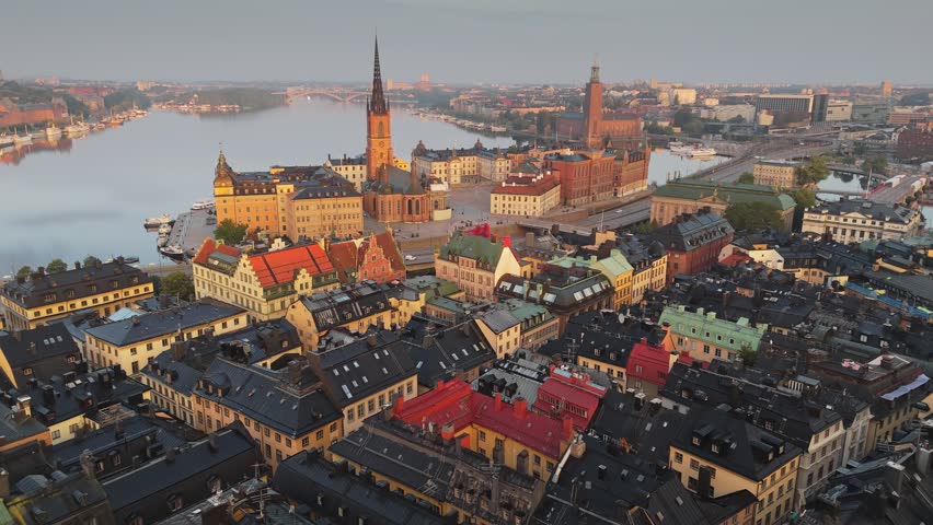 Aerial view of Stockholm old town at sunrise, the camera flies over rooftops towards Riddarholmen church. Scenic morning panorama shows the Swedish capital and calm water. Stockholm, Sweden