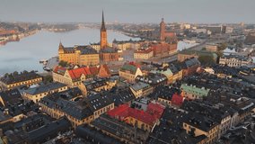 Aerial view of Stockholm old town at sunrise, the camera flies over rooftops towards Riddarholmen church. Scenic morning panorama shows the Swedish capital and calm water. Stockholm, Sweden - Powered by Shutterstock - Get 15% off with code: PIKWIZARD15