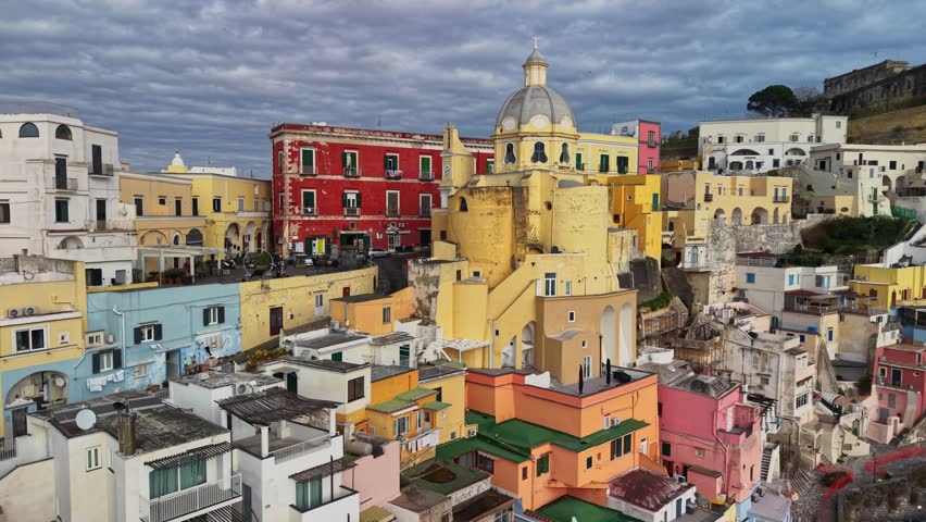 Aerial view shows colorful houses in Corricella harbor on Procida island, beautiful architecture is visible. Local boats are docked in the Mediterranean water. Italian island Procida, Naples